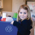 Young girl holding recycle bin full of plastic bottles and cardboard